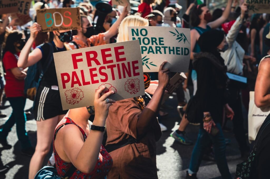 مظاهرة سلمية لدعم فلسطين في شوارع المدينة عام 2025، يظهر المشاركون وهم يحملون أعلام فلسطين ولافتات داعمة، ويشارك فيها رجال ونساء وأطفال، بمظهر حيوي وواقعي، يعكس الدعم الشعبي للقضية الفلسطينية.